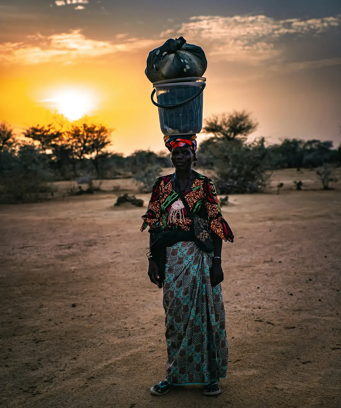 A woman carries water on her head at sunset
