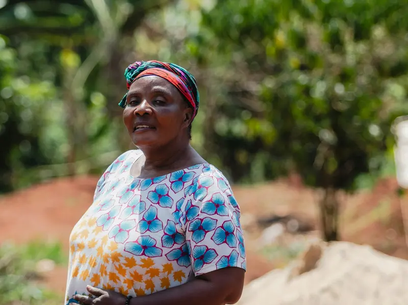 A smiling Ugandan woman stands in a garden